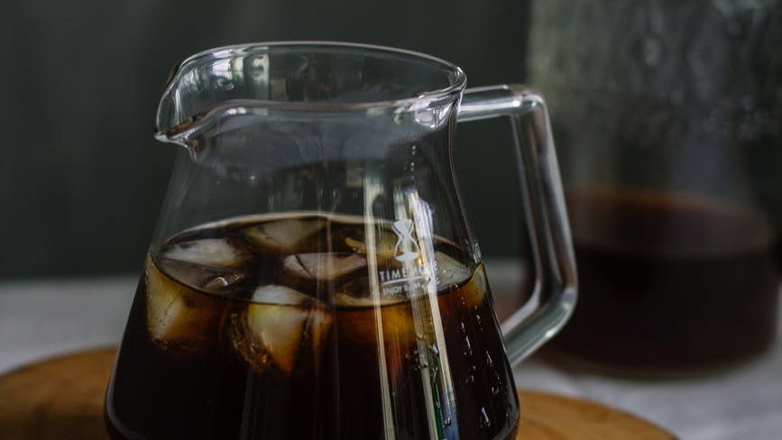 clear glass pitcher with cola and ice on wooden chopping board